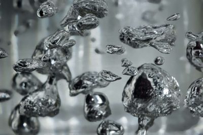 Drops and bubbles of mercury in water close-up. Dangerous chemical element, the scientific experience. Defocused image, motion blur